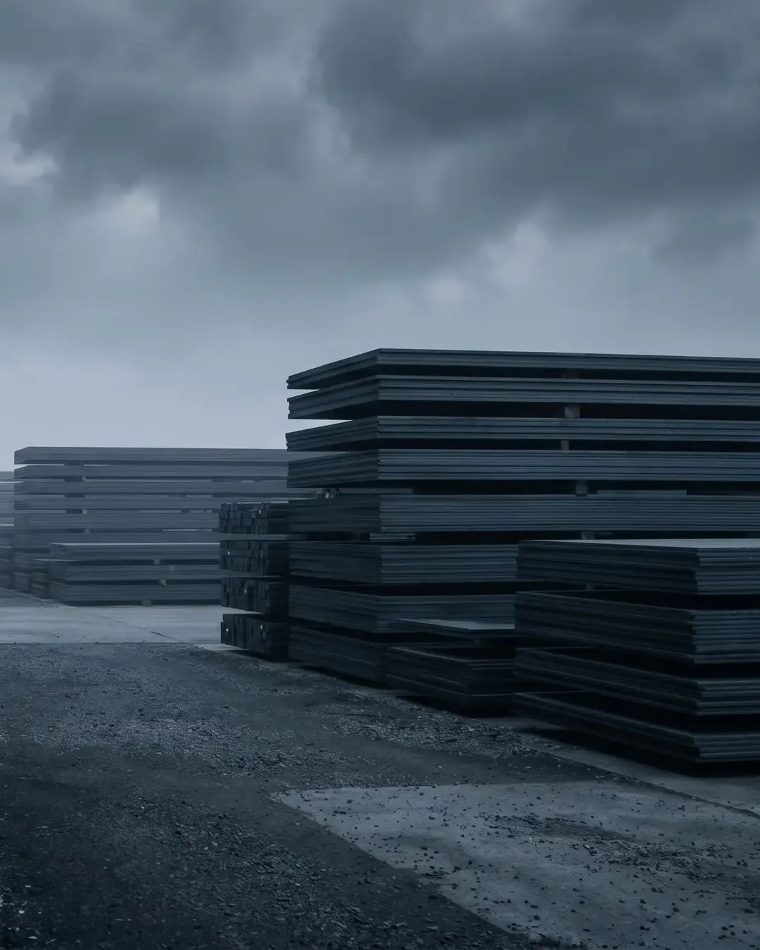 A neatly stacked yard of cut steel plate and billet under a heavy grey sky