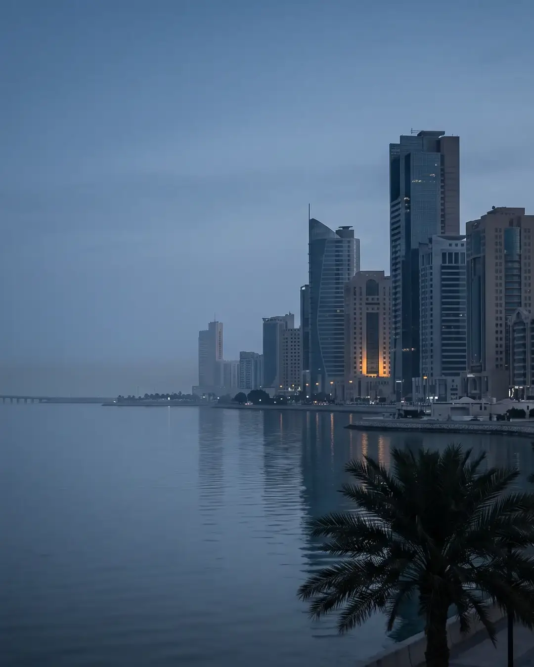 The Khobar corniche at blue hour: the Eastern Province seafront towers above the Gulf, the causeway receding into haze